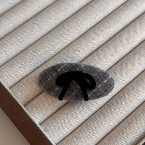 Close-up of grey tweed oval hair clip with plaid pattern and black velvet bow ornament