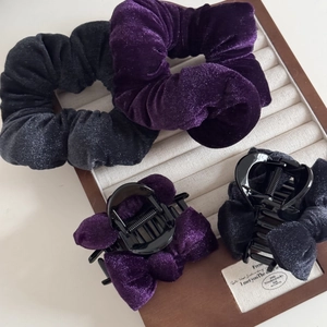 Detail view of purple and grey velvet scrunchies and bow hair clips in a jewelry tray
