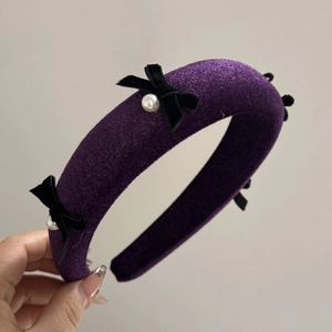 Detail of dark purple velvet headband featuring elegant black bows and faux pearls