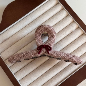 Detail of tweed hair claw clip with dark red velvet bow on beige striped display tray