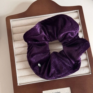 Detail of deep purple velvet hair scrunchie with silver LOVE metal tag on a tray
