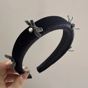 Close-up of velvet headband featuring grey bows and white pearls on black fabric texture