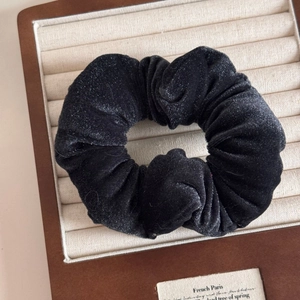 Close-up of black velvet scrunchie with soft sheen and rich pleated texture in a display box