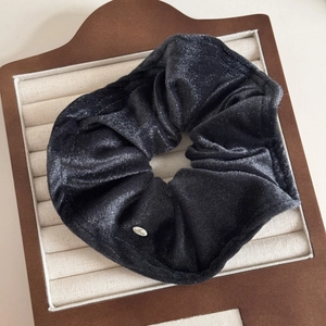 Detail view of black velvet hair scrunchie with glitter effect and silver Love metal tag