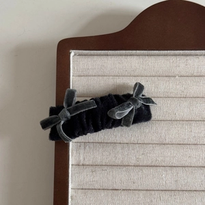 Close-up of a vintage black velvet hair clip with two grey bows on a fabric display board