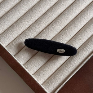 Detail view of a black velvet hair clip featuring a silver oval Love engraved metal plate