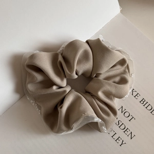 Close-up of khaki scrunchie with white mesh trim and delicate pearl bead accents