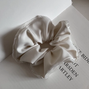 Macro shot of cream satin scrunchie featuring elegant lace edges and glossy fabric texture