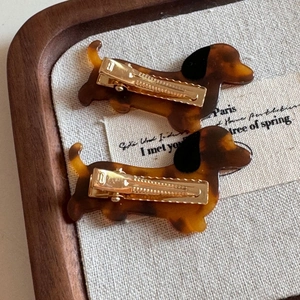 Detailed macro view of two tortoiseshell dachshund hair clips with golden metal duckbill grips