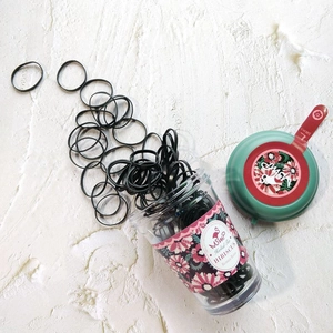 Détail de 130 élastiques à cheveux noirs dans un flacon style infusion florale