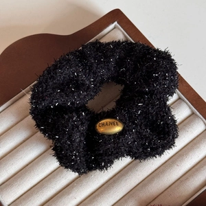 Detail of black plush scrunchie with silver sparkles and a golden oval metal logo plate