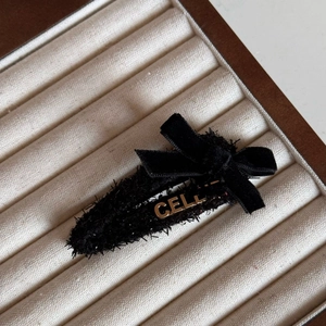 Close-up of black velvet bow hair clip with gold metal letter logo on white box