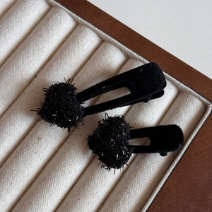 Detail view of black velvet hair clips with glittery pompoms on a wooden jewelry tray