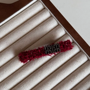 Detail of burgundy plush hair clip with sparkling crystal letter logo on display tray