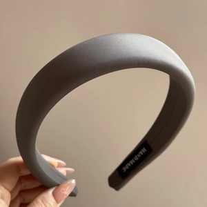 Macro shot of dark grey padded satin headband showing handmade label and premium texture