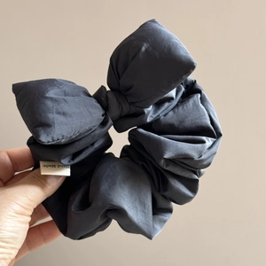 Detail of black satin bow scrunchie featuring a white Hand Made textile label