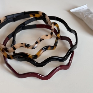 Detail view of four glossy wavy cellulose acetate headbands in tortoiseshell and solid colors