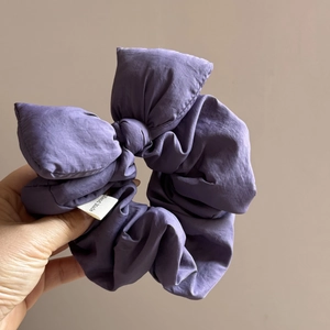 Detail of purple padded bow scrunchie with wrinkled fabric and Hand Made woven label