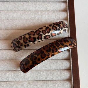 Close-up of two leopard print acetate hair clips on a beige velvet jewelry display tray