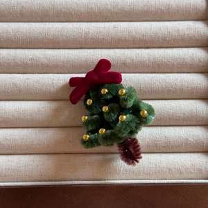 Detail of handmade Christmas tree hair clip with green plush branches and a red velvet bow