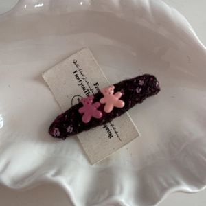 Close-up of knit fabric hair clip with two pink resin bear charms on a ceramic plate