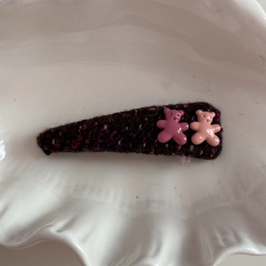Detailed view of a purple knitted hair clip with two cute plastic bears on white plate