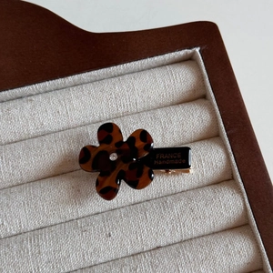 Detailed close-up of leopard pattern flower hair clip with silver rhinestone in wood box