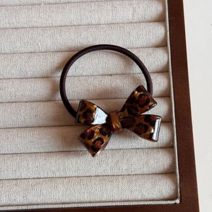 Close-up of leopard print bow hair tie with high elastic band on a cream fabric base