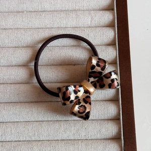 Detail view of a vintage leopard print bow hair tie on a beige velvet jewelry display tray