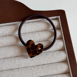 Macro detail of leopard print heart hair clip with a sparkling rhinestone on wood stand