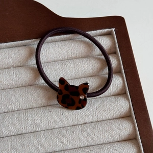 Detail of leopard print cat charm hair tie with crystal eye on beige velvet tray