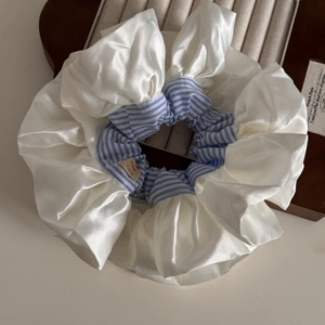 Macro detail of cream satin and blue striped oversized scrunchie with handmade tag