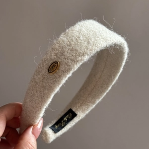 Gros plan du serre-tête en peluche crème avec un médaillon métallique doré