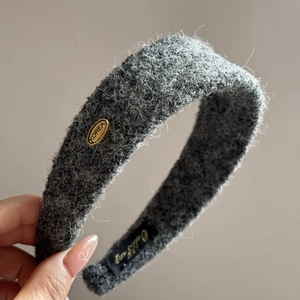 Gros plan d'un serre-tête gris en peluche avec plaque dorée et texture en tricot