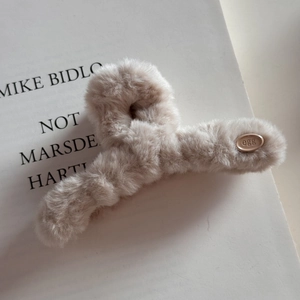 Gros plan d'une pince à cheveux en peluche beige avec étiquette dorée et fourrure douce