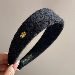 Détail d'un serre-tête en peluche noire avec texture tricotée et plaque dorée Korea