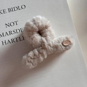 Détail d'une grande pince à cheveux en peluche crème avec étiquette ovale sur fond de livre