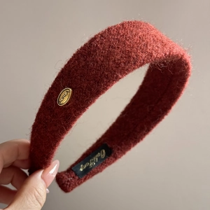 Détail du serre-tête d'hiver en peluche rouge brique avec logo métallique doré