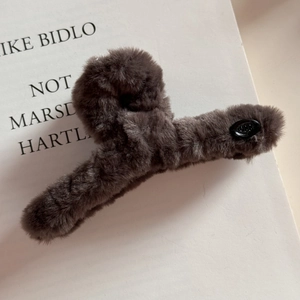 Détail d'une pince à cheveux en peluche marron café avec ornement ovale et texture douce