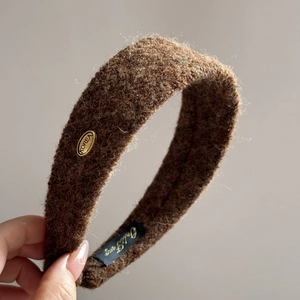 Détail du serre-tête en tricot marron avec un emblème en métal doré élégant