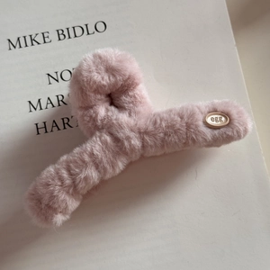 Détail de la pince à cheveux en peluche rose avec petit logo egg en métal sur un livre