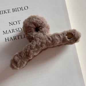Détail d'une pince à cheveux en peluche marron avec étiquette métallique ovale egg