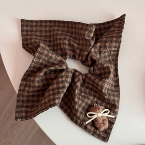 Detail of checkered scrunchie with a brown plush bear and a beige ribbon bow accessory