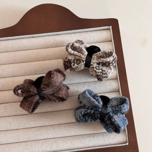 Three tweed bow hair clips in brown, khaki, and denim blue displayed on a jewelry tray