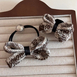 Detail of tweed bow hair clip and elastic tie set with pearl accent on velvet board