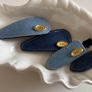 Denim blue hair clips with oval gold metal tags featuring egg engraving in a shell tray