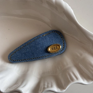 Close-up of denim BB clip with yellow stitching and oval gold-tone metal egg tag