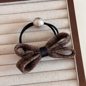 Detailed close-up of a tweed bow hair tie with a silver-gray pearl bead on velvet