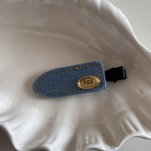Detailed macro view of denim blue hair clip with golden egg metal plate on white plate