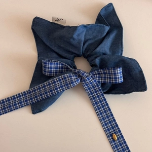 Close-up of blue denim scrunchie with plaid bow and engraved gold metal love pendant